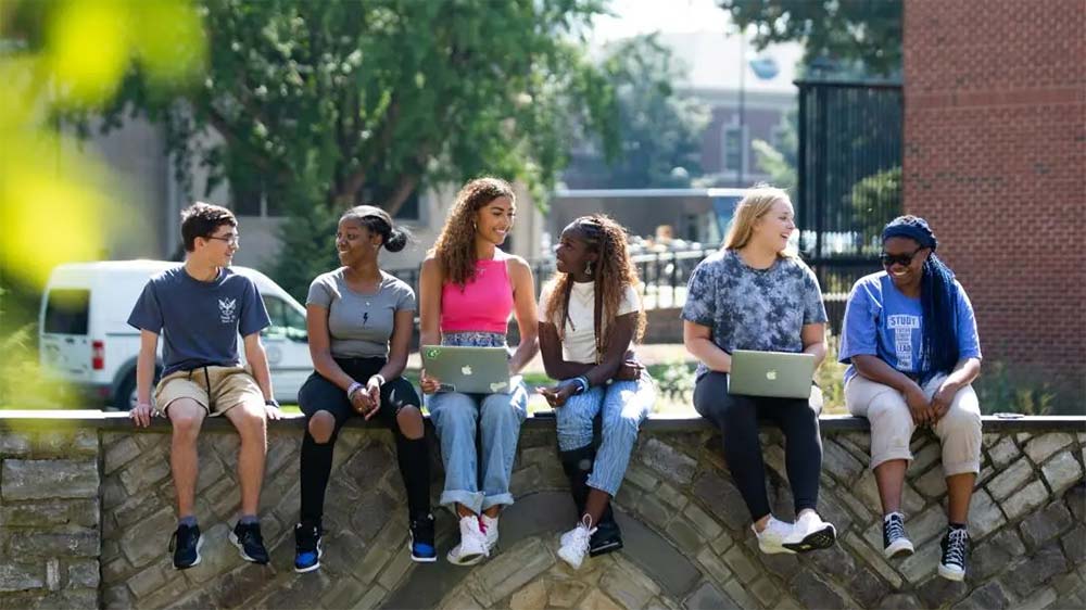 A group of students pose for a photo sitting on a low wall.