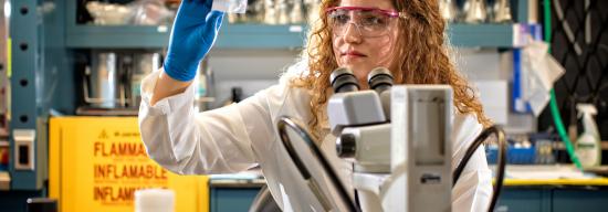 Female student in a lab coat analyzing a medicinal substance