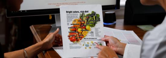 Two people looking at a paper with fruits and vegetables advising people on what to eat