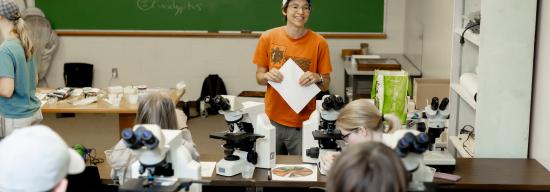 Student explaining a STEM concept while standing in front of a green chalkboard