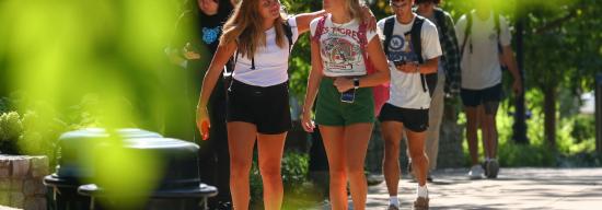 One female student putting her arm over another female student during a conversation outside