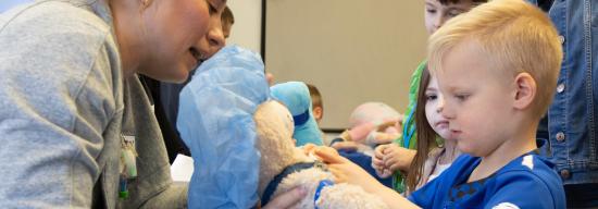 Child with teddy bear inside hospital setting.