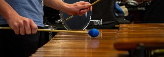 Student using musical tools to hit a wooden marimba