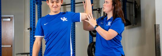 Female athletic trainer helping a male student athlete with their range of motion