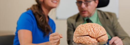 Female student in a lab coat talking with professor about a brain sculpture