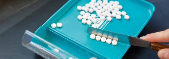 Student scraping medicinal pills off a teal tray
