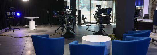 Journalism studio with blue chairs, lights, televisions, and cameras