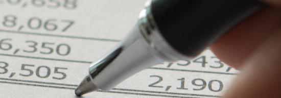 Person writing down notes on a sheet of paper filled with numbers