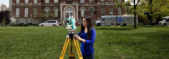 Student working with an engineering item in front of a classroom building