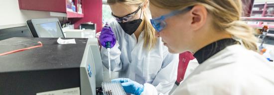 Two females in lab coats inserting a substance into plastic medical tools