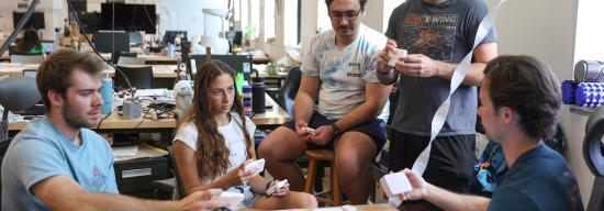 Several students surrounding a desk discussing a design project