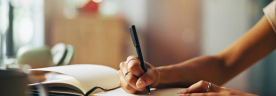 Student writing with a black pen on a notebook