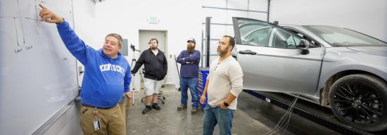 Teacher instructing students in a garage with a car.