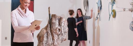 Female student on her iPad in front of a tree piece
