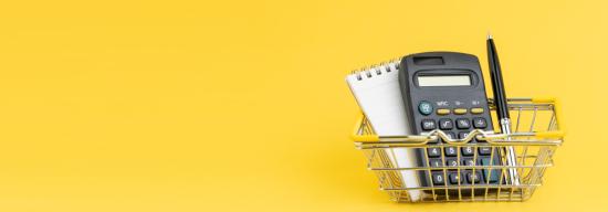 A small metal shopping basket containing a calculator, a notepad, and a pen against a yellow background.