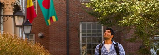 Male student walking on campus underneath a country's flag