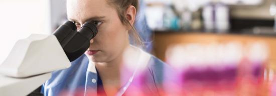 Female closely inspecting a substance through a microscope
